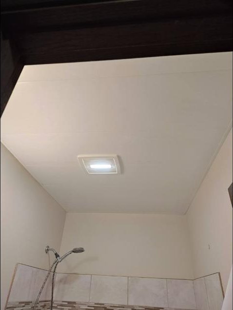 Bathroom mid-renovation with fresh ceiling panels above a shower